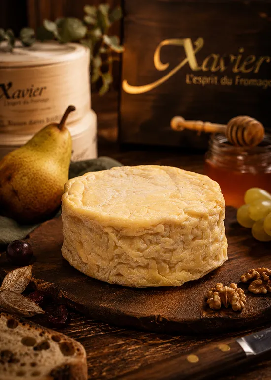 Fromage Xavier artisanal pos&eacute; sur planche en bois avec fruits et &eacute;pices